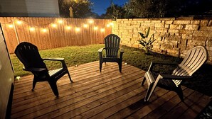 En træterrasse med tre Adirondack-stole, en stenvæg og lyskæder.