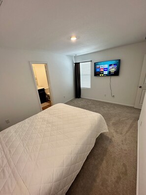 Un dormitorio con una cama, televisión montada en la pared y una ventana con persianas.