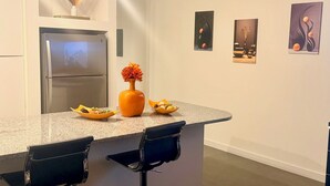 Eine moderne Küche mit einer Granitabdeckung, zwei Barhocker, einem Kühlschrank und drei gerahmten Kunstwerken an der Wand.