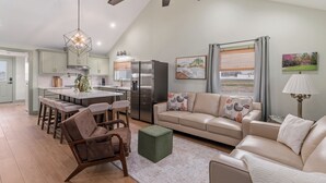 A modern kitchen with a central island, bar stools, and a dining table. There is a beige sofa with patterned cushions and a small green ottoman. - Charming 2 Bedroom 2 Bath Cottage near the lake. (Campbellsville)