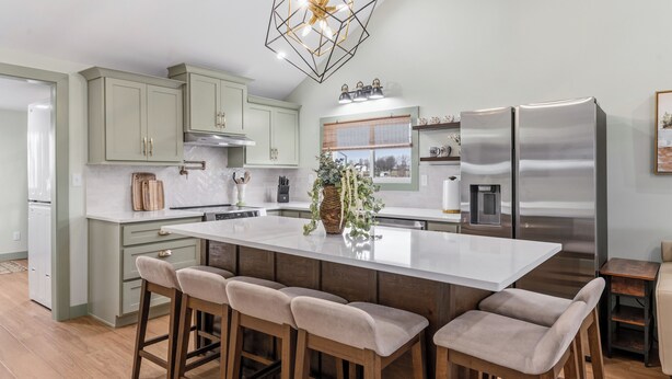 A modern kitchen with a large island, bar stools, stainless steel appliances, and a decorative plant. - Charming 2 Bedroom 2 Bath Cottage near the lake. (Campbellsville)