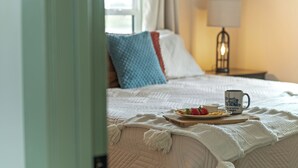 A neatly made bed with a white quilt, a tray with breakfast items, and a mug on the bed. - Charming 2 Bedroom 2 Bath Cottage near the lake. (Campbellsville)