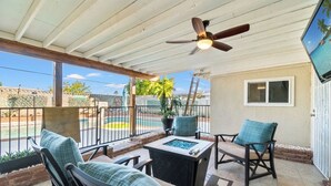 Ein überdachter Patio-Bereich mit Gartenmöbeln, einem Deckenventilator und Blick auf einen Swimmingpool.