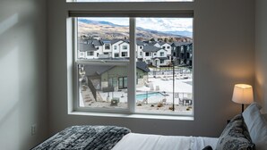 Un dormitorio con un amplio ventanal con vistas a una zona residencial y una piscina.