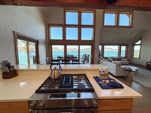 A modern kitchen with a gas stove, a kettle, and a dining area with a view of the sea.