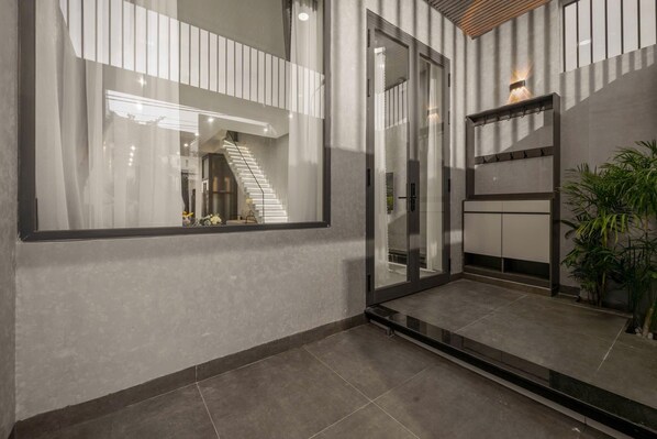 A modern interior with a glass door entrance, a staircase, and a potted plant. - Amelia (Da Nang)