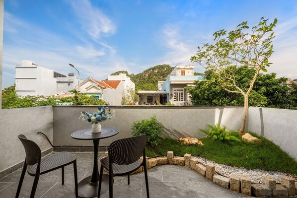 Une terrasse avec deux chaises et une table, un petit arbre, et une vue sur des bâtiments et des collines en arrière-plan.