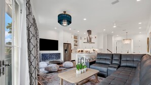 A modern living room with a sectional sofa, a wooden coffee table, and a TV mounted on the wall. - Live in Luxury at This Brand New Tybee Island Escape | Heated Pool Access (Tybee Island)