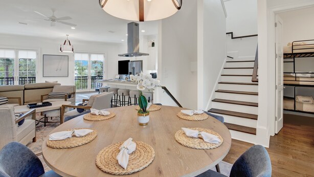 A modern living room with a round dining table, sofas, and a staircase. - Live in Luxury at This Brand New Tybee Island Escape | Heated Pool Access (Tybee Island)