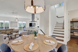 A modern living room with a round dining table, sofas, and a staircase. - Live in Luxury at This Brand New Tybee Island Escape | Heated Pool Access (Tybee Island)