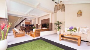 A spacious living area with a sofa set, a coffee table, and a dining table. There is a staircase leading to an upper level. - Red Lotus Villa Seminyak (Seminyak)