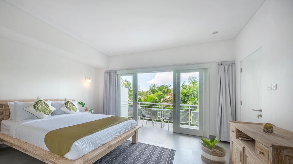 A hotel room with a bed, a balcony, and a view of greenery.