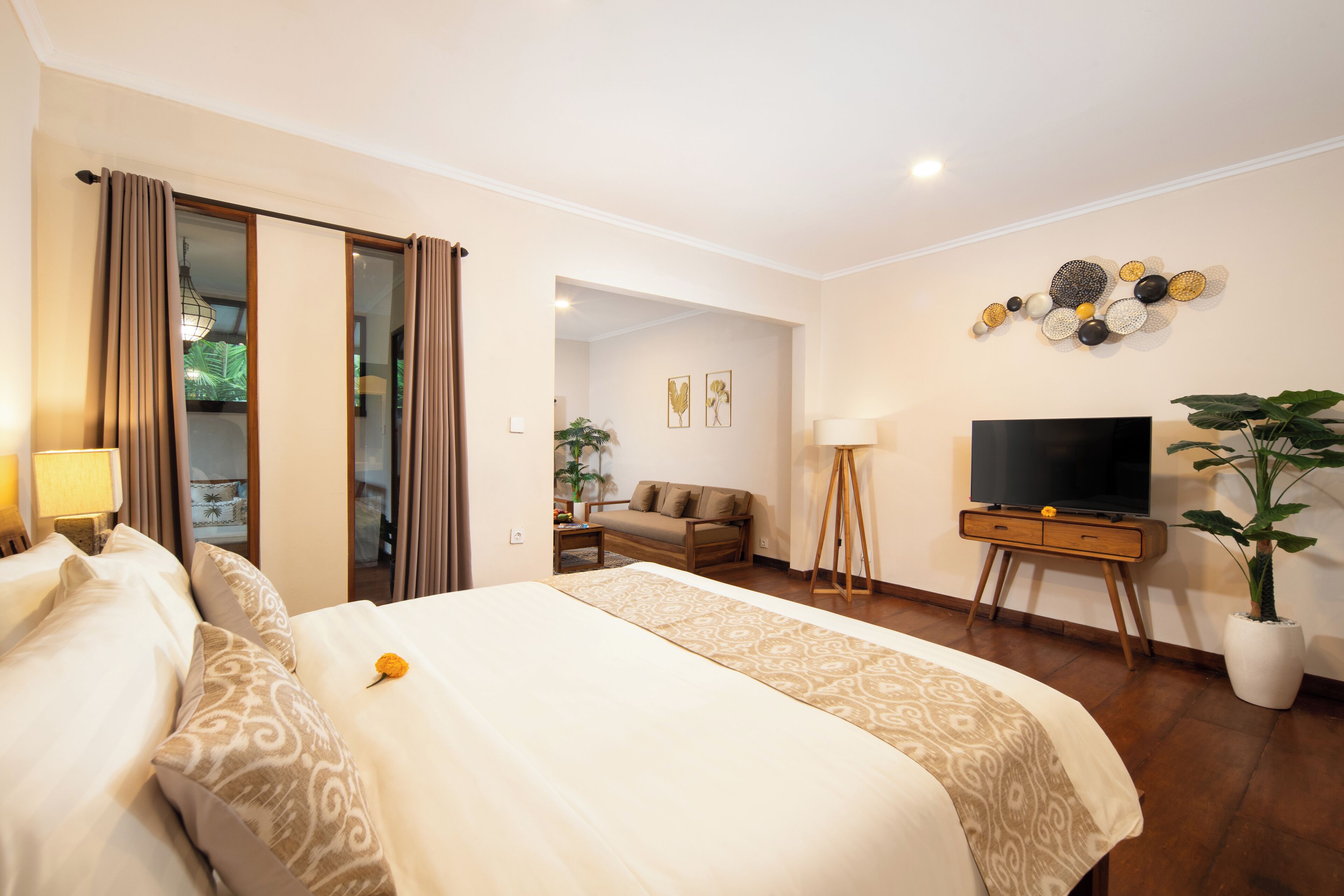 Habitación de hotel con una cama grande, un televisor sobre un mueble de madera, una planta en maceta y vistas al exterior.