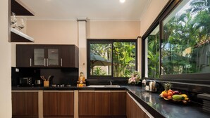 A modern kitchen with dark wood cabinets, a stainless steel refrigerator, and a large window offering a view of greenery. - Red Lotus Villa Seminyak (Seminyak)