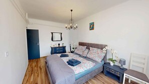 A bedroom with a bed, bedside tables, a dresser, a chandelier, and a door. - Holiday apartment with pool, whirlpool, sauna and hot tub (Balatonszabadi)