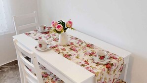A white table with a floral tablecloth, two white chairs, and a vase with pink flowers. - Holiday apartment with pool, whirlpool, sauna and hot tub (Balatonszabadi)