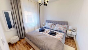 A bedroom with a bed, a nightstand, a lamp, a clock, and a window with curtains. - Holiday apartment with pool, whirlpool, sauna and hot tub (Balatonszabadi)
