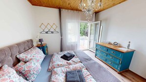 A bedroom with a bed, a dresser, a chandelier, and a window. - Holiday apartment with sauna, pool, hot tub and bathing barrel (Balatonszabadi)