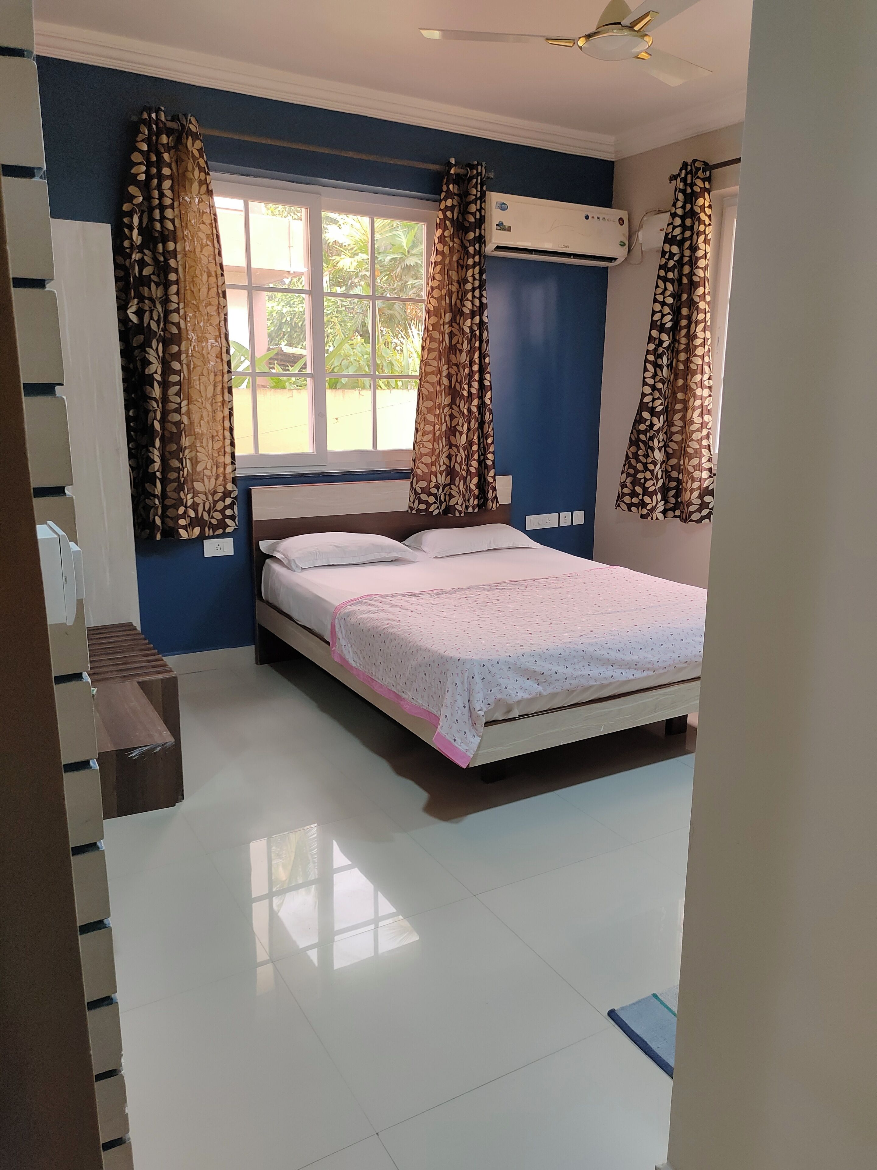 A bedroom with a bed, a window with curtains, an air conditioning unit, and a ceiling fan.