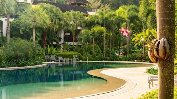 A swimming pool surrounded by lush greenery and a traditional-style building in the background.