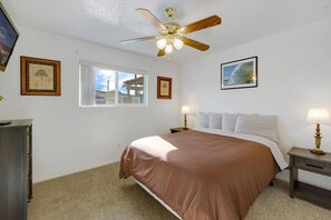 Een slaapkamer met een bed, een plafondventilator, een raam en ingelijste foto’s aan de muur.