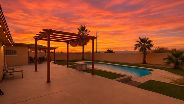Un espacio al aire libre techado con piscina, palmeras y un atardecer.