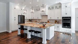 A modern kitchen with white cabinets, a central island with bar stools, pendant lighting, and a built-in oven. - Contour - Priv Pool- Fun Design- Mins 2 everything (Phoenix)