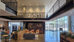 Eine geräumige Lobby mit einer Galerieebene, Sitzbereichen und einem großen Bücherregal.