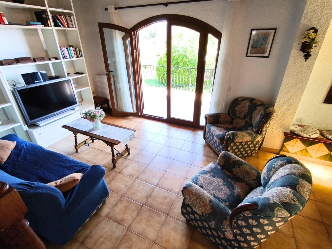 A living room with a sofa, armchairs, a coffee table, a TV, and a bookshelf.