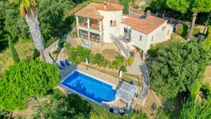 Una casa de dos pisos con piscina, rodeada de exuberante vegetación y árboles.
