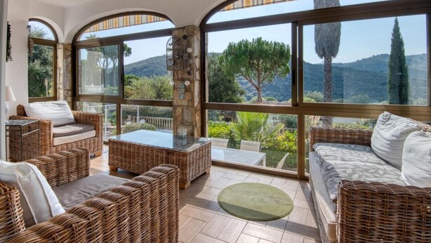Una habitaci ón iluminada por el sol con muebles de mimbre, ventanas amplias y un pilar de piedra.
