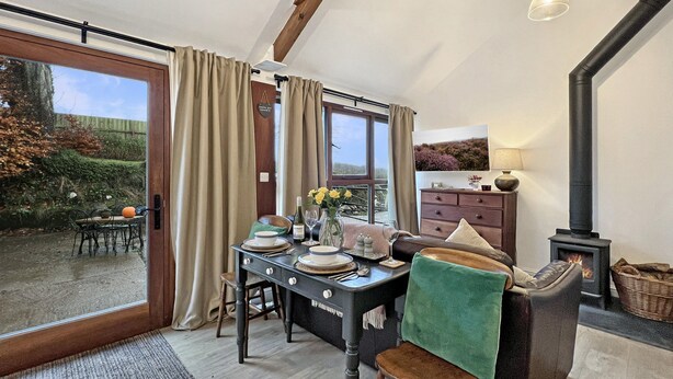 A dining area with a table set for two, a fireplace, and a view of the outdoors. - Daveys Barn, Brendon Hill on Exmoor (Nr Watchet)