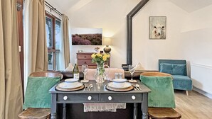 A dining area with a table set for two, a sofa, and a painting on the wall. - Daveys Barn, Brendon Hill on Exmoor (Nr Watchet)