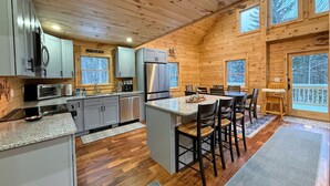Une cuisine chaleureuse, aménagée dans le style d’un chalet, avec des murs en bois, un plan de travail en granit et un îlot central doté de tabourets de bar.