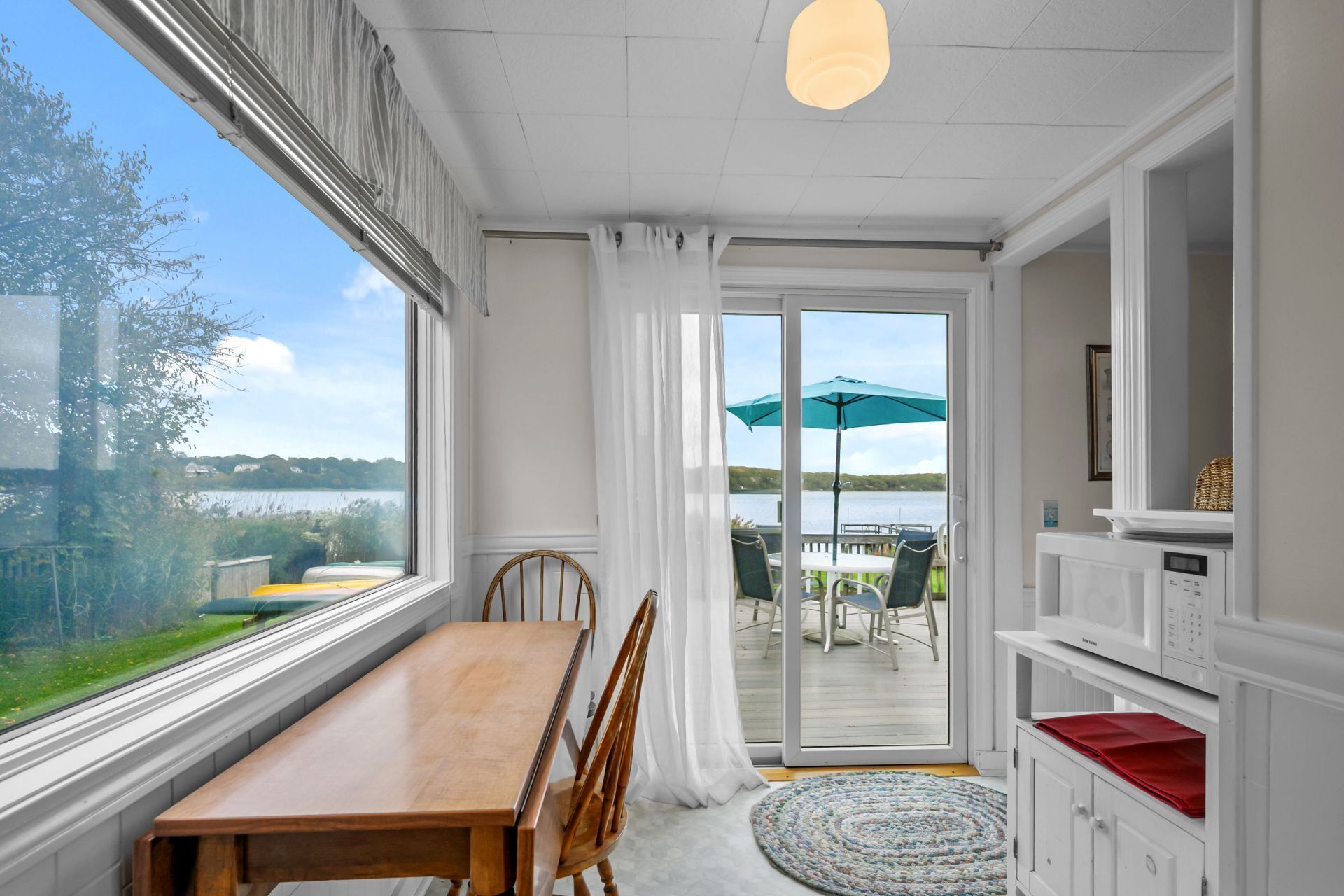 A room with a wooden table and chairs, a sliding glass door leading to an outdoor area with a table and chairs, and a view of a body of water.
