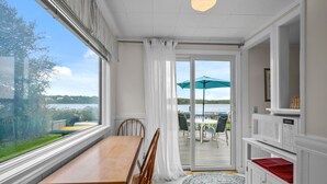 A room with a wooden table and chairs, a sliding glass door leading to an outdoor area with a table and chairs, and a view of a body of water. - Tranquil Eastham Waterfront Cottage Escape (Eastham)