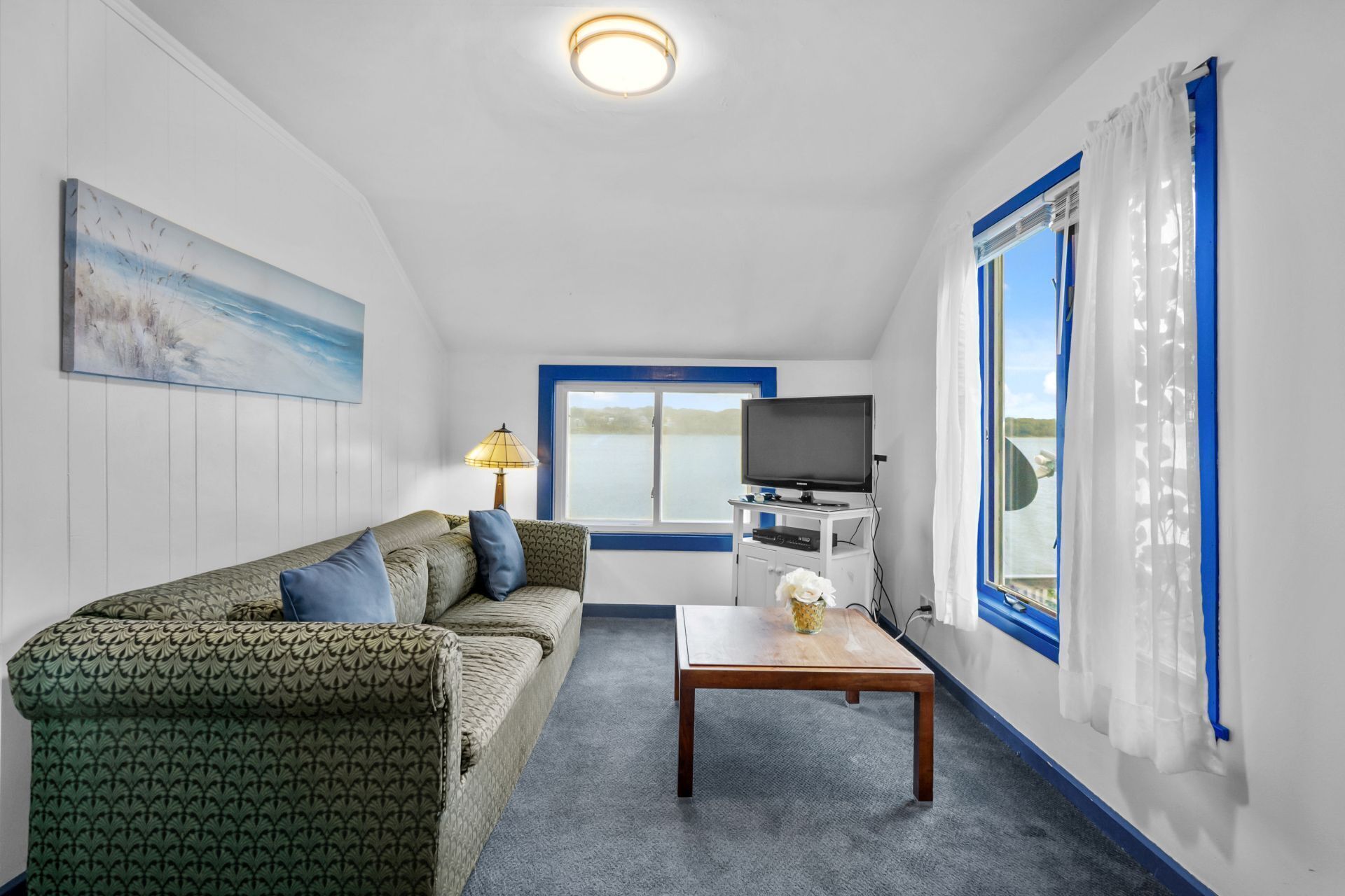 A room with a sofa, a table, a TV, and a window with curtains.