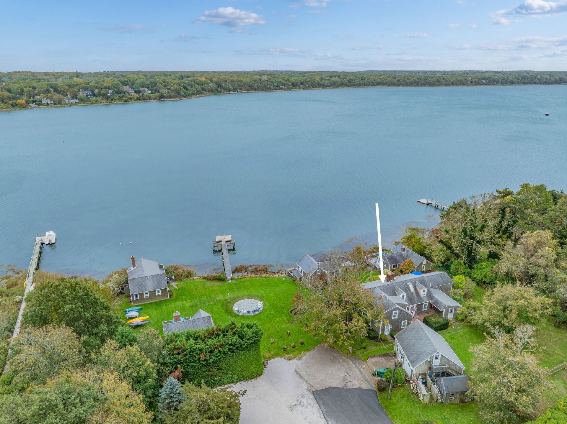 An aerial view of a lakeside property with a dock, a circular lawn feature, and a house with a sloped roof.