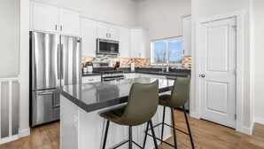 A modern kitchen with white cabinetry, stainless steel appliances, and a central island with bar stools. - Wasatch Ridge Retreat | Central | Fenced Backyard (Orem)