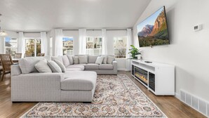A modern living room with a sectional sofa, a fireplace, and a large window with curtains. - Wasatch Ridge Retreat | Central | Fenced Backyard (Orem)