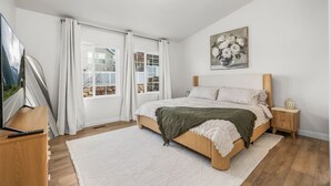 A bedroom with a bed, a nightstand, a TV, and a window with curtains. - Wasatch Ridge Retreat | Central | Fenced Backyard (Orem)