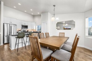 A modern kitchen with white cabinets, a stainless steel refrigerator, and a dining area with a wooden table and chairs.