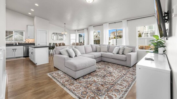 A modern living room with a grey sectional sofa, a patterned rug, and a flat-screen TV on a white stand. - Wasatch Ridge Retreat | Central | Fenced Backyard (Orem)