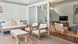 Una habitación con un sofá blanco, sillas de madera, una mesa de centro y un ventilador de techo.