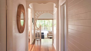 Un pasillo con suelo de madera, una puerta blanca y un espejo ovalado de madera.