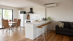 Una cocina moderna con una isla central, taburetes de bar y un comedor con sillas de mimbre.