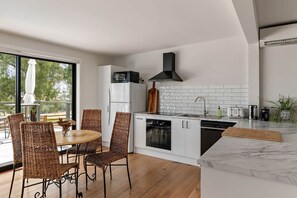 A modern kitchen with white cabinets, a black range hood, a microwave, and a dishwasher. There is a dining area with wicker chairs and a table. - An Unforgettable View (Dixons Creek)