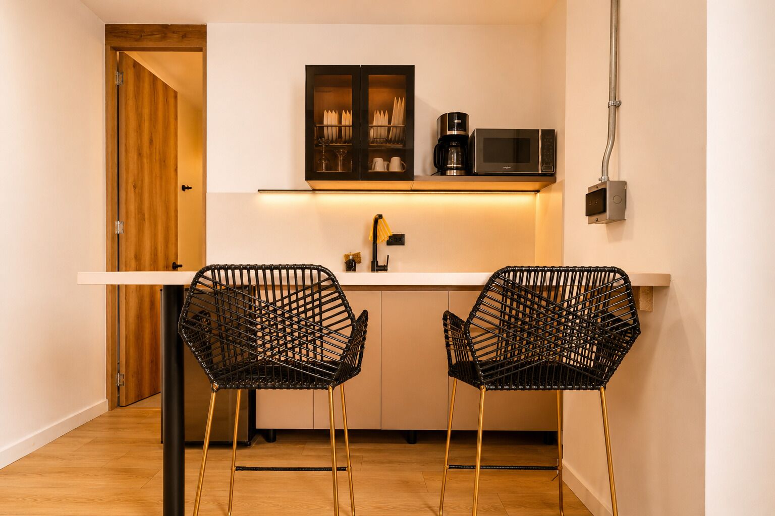 A compact kitchen with two black wireframe chairs, a microwave, and a coffee maker on a white countertop.