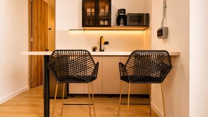 Une cuisine compacte avec deux chaises à armature métallique noire, un four à micro-ondes et une machine à café, le tout posé sur un plan de travail blanc.