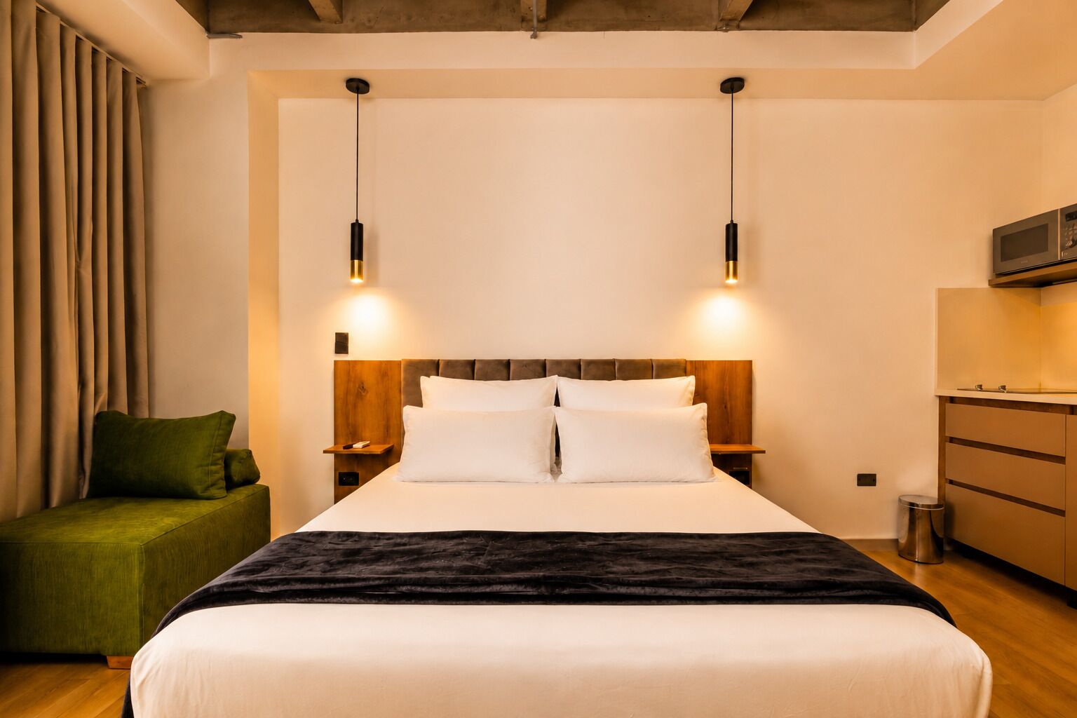 A hotel room with a bed, bedside tables, a green armchair, a wooden headboard, and a microwave.
